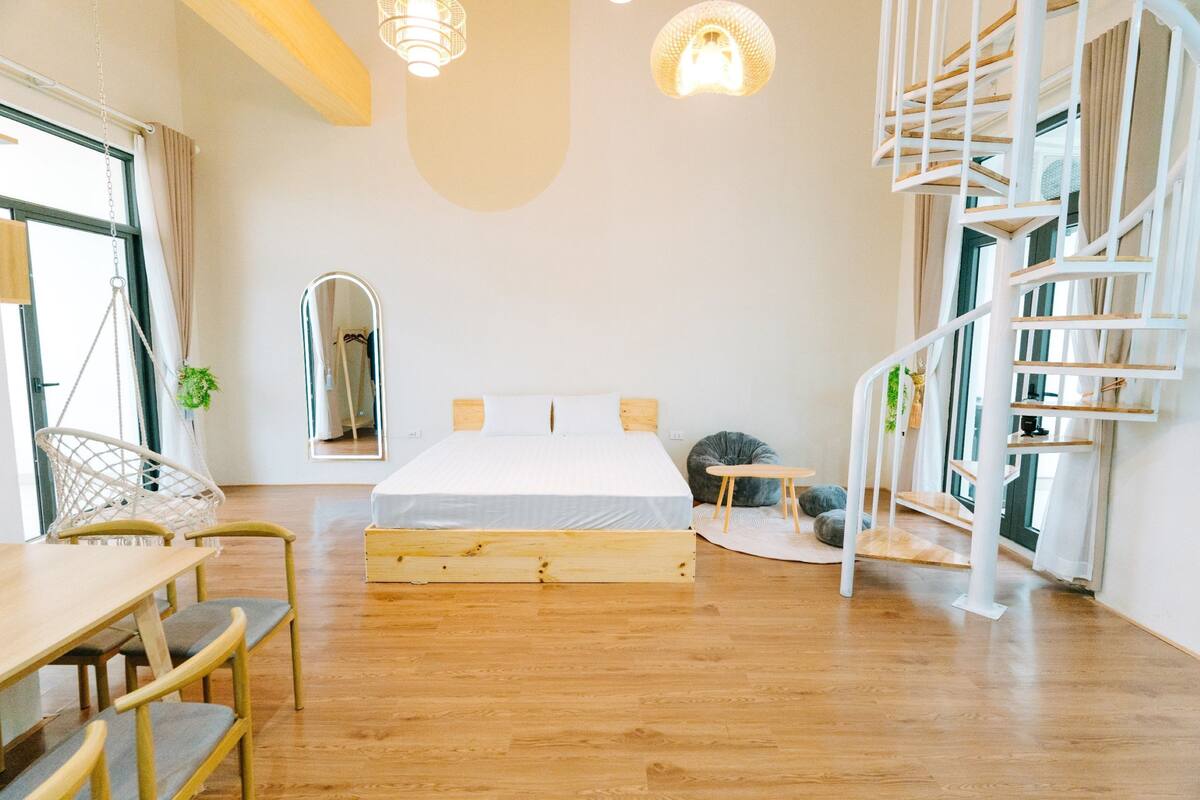 Quarto moderno com cama de madeira, escada em espiral e área de refeições com mesa e cadeiras.