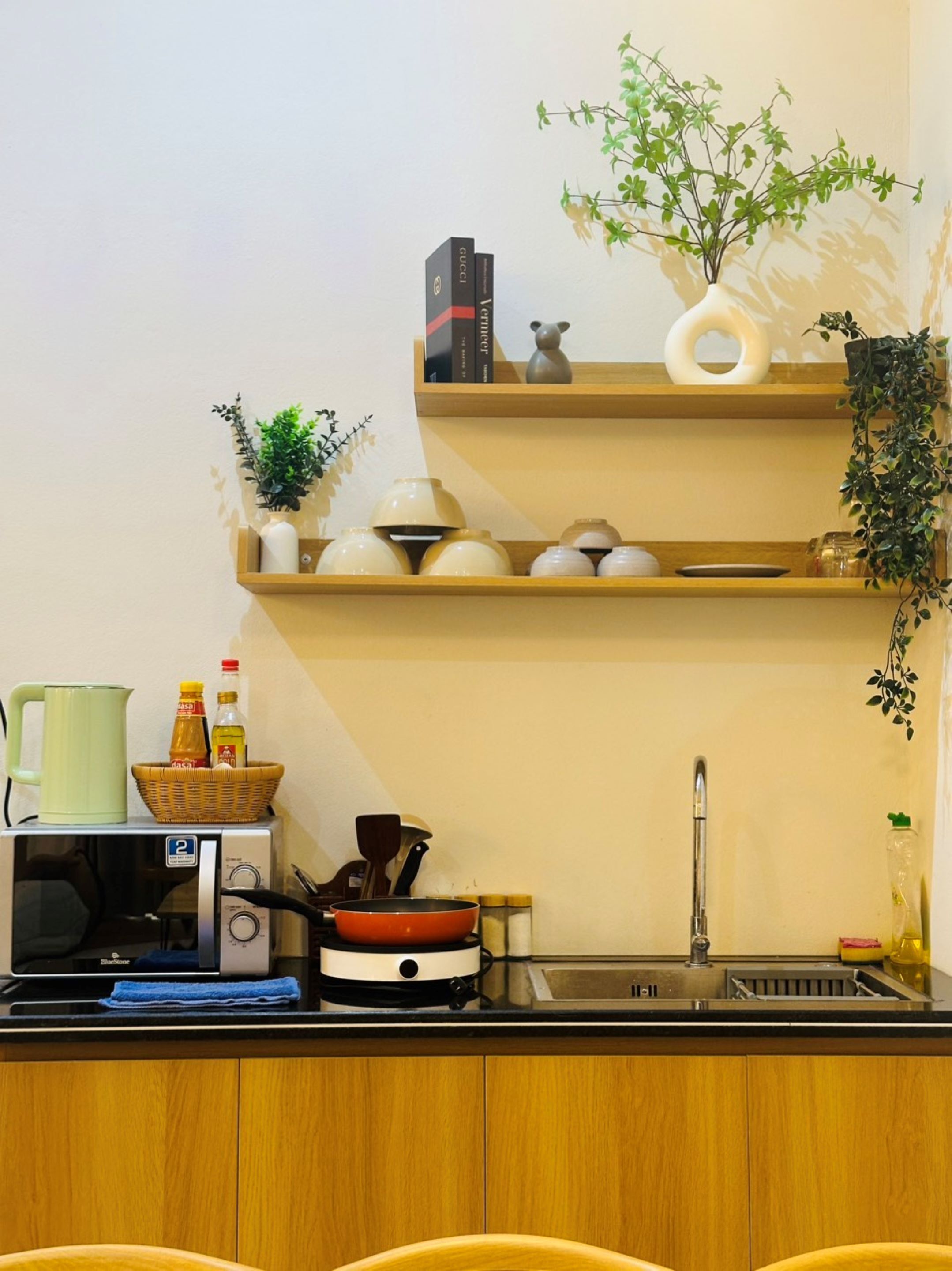 A compact kitchen with wooden cabinets, a microwave, a kettle, a sink, and various kitchen utensils.