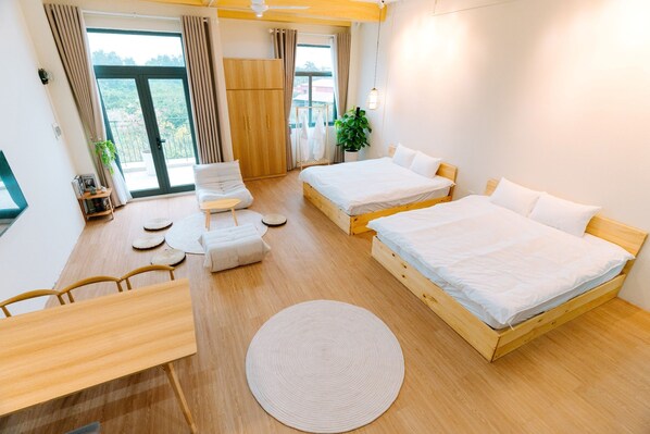 Una habitación de hotel moderna con dos camas, un escritorio de madera, un tapete redondo y un balcón con vistas a zonas verdes.