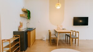 A compact living space with a kitchenette, a dining area with a table and chairs, a bed, and a TV mounted on the wall. - X-Stay (Hai Phong)