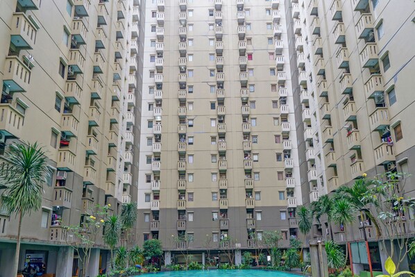 A high-rise residential building with multiple balconies, a central courtyard, and surrounding greenery.