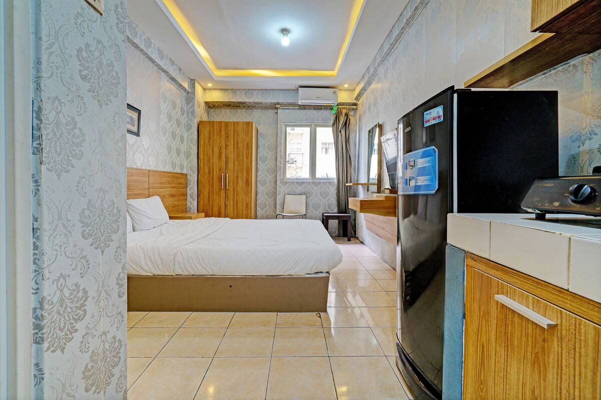 A hotel room with a bed, a refrigerator, a wooden cabinet, and a window with curtains.