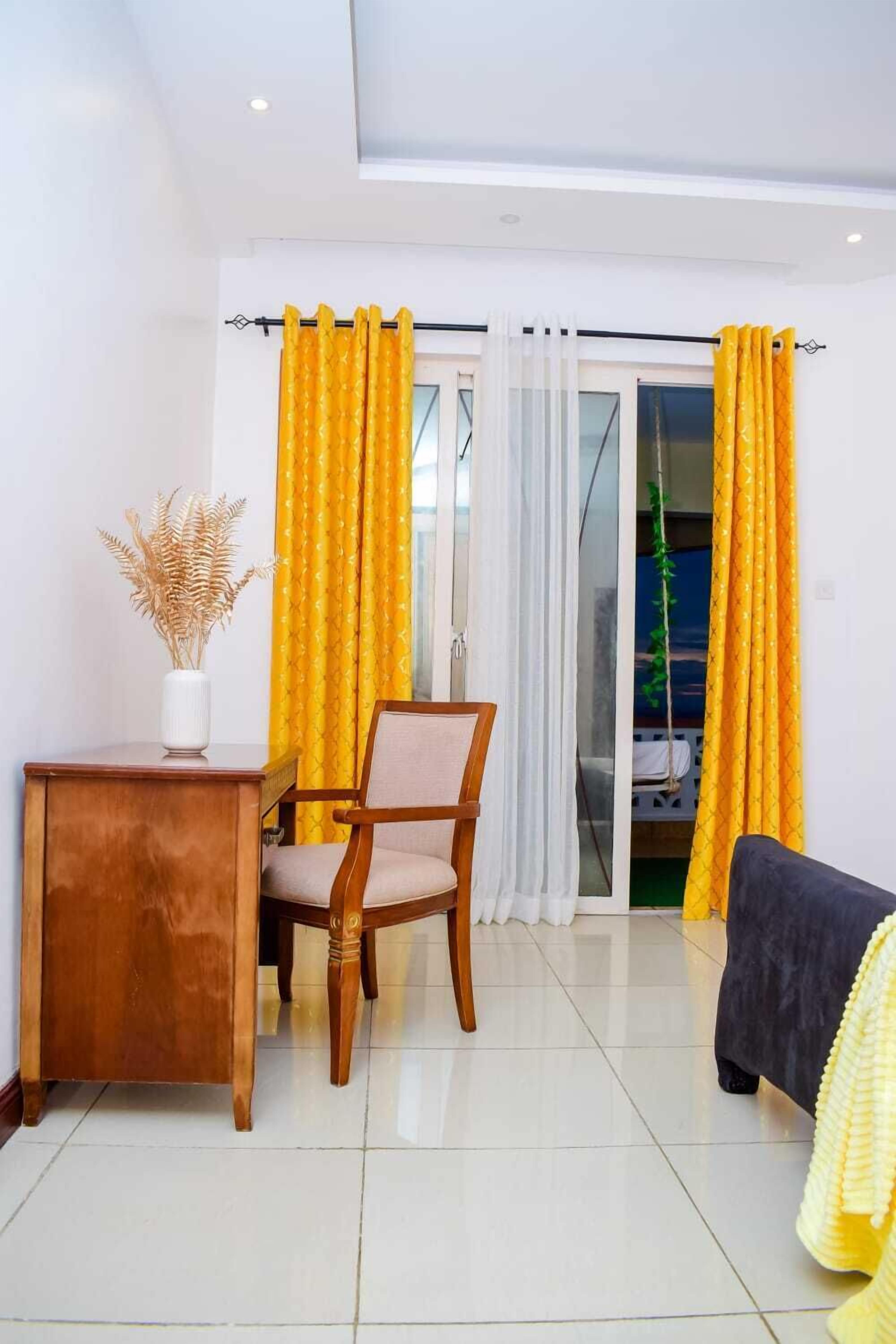 A room with a wooden desk, a chair, a sofa, and a sliding glass door with yellow curtains.