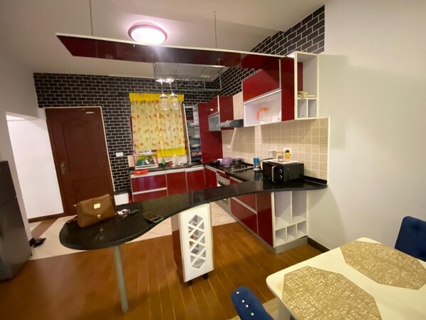 A compact kitchen with a central island, red and white cabinetry, and a black backsplash.