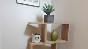 Uma estante de canto com várias prateleiras, um quadro emoldurado e um vaso com planta.