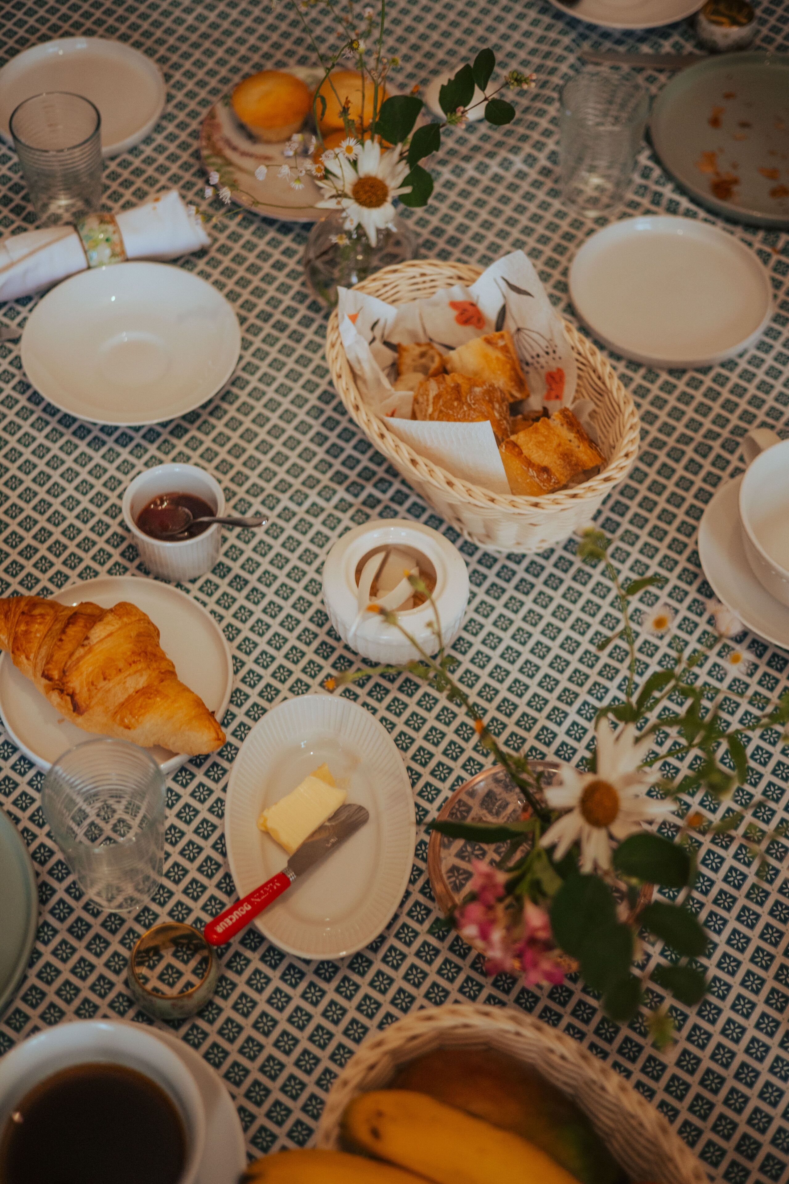 A table set with plates, a basket of bread, a vase with flowers, and a small bowl of jam.