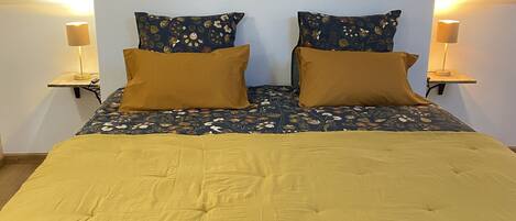A neatly made bed with a floral-patterned duvet and two mustard-colored pillows, flanked by two bedside lamps on matching nightstands.