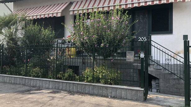 Un edificio con un número, una entrada protegida por una reja y una escalera que lleva a la puerta principal.