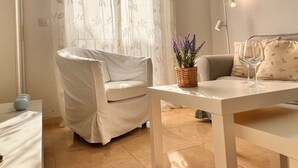 Una habitación acogedora con una silla tapizada, una mesa con una planta en maceta y un sofá con cojines.