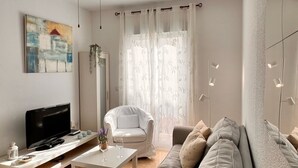 Una sala de estar moderna con un televisor de pantalla plana, un sofá blanco, un sillón blanco y una mesa de comedor.