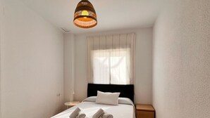Un dormitorio minimalista con una cama, una mesita de noche, una lámpara y un aplique.