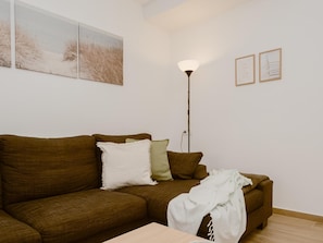 Un salon avec un canapé marron, un lampadaire et deux tableaux encadrés accrochés au mur.