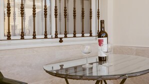 Una mesa de vidrio con una botella de vino y dos copas, una ventana con barandilla de metal y vistas de edificios.