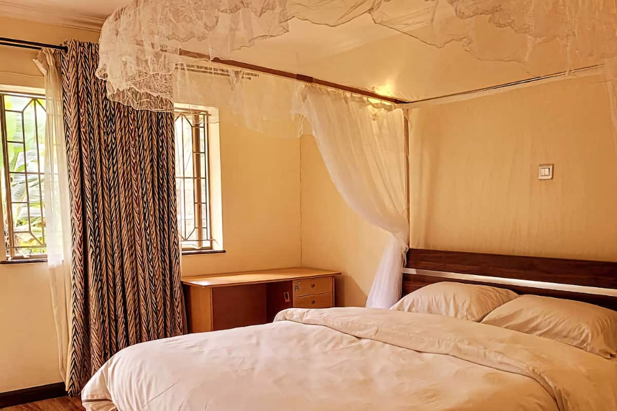 Une chambre à coucher avec un lit en bois, une table de chevet, une fenêtre avec des rideaux et un plafond agrémenté d’un dais décoratif.