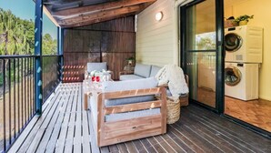Un terrazzo in legno con un divano e un tavolo, una lavatrice e una porta scorrevole in vetro che dà su un ambiente interno.