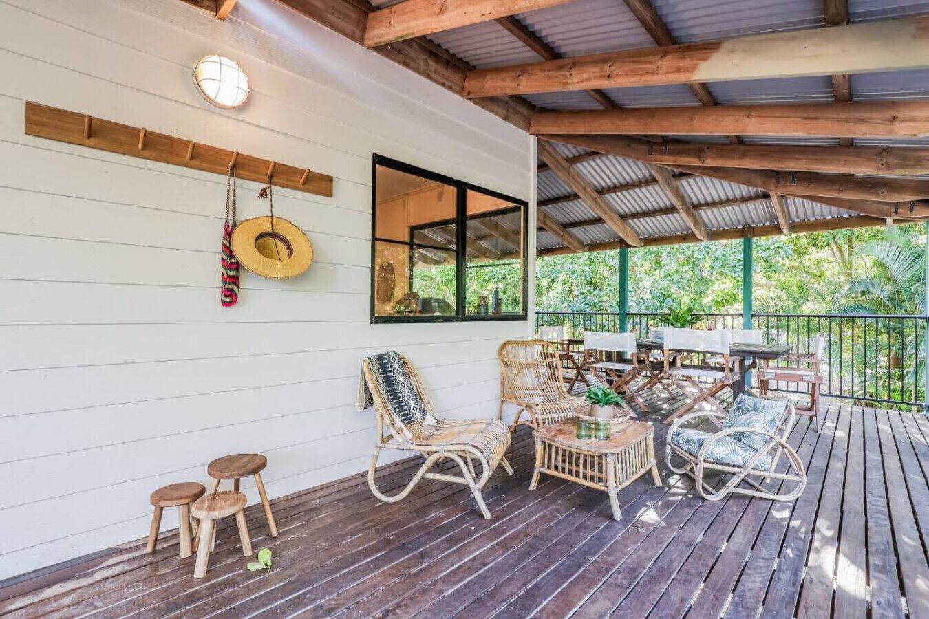 A covered outdoor area with wooden flooring, wicker furniture, and a view of greenery.