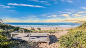 Una spiaggia con una passerella di legno che conduce alla riva, circondata da vegetazione.