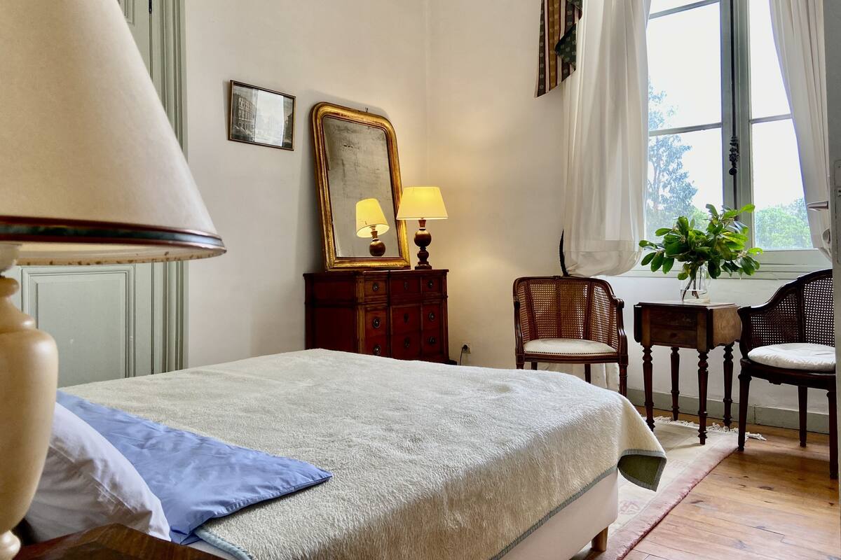A bedroom with a bed, a dresser, a chair, a desk, a mirror, and a window with curtains.
