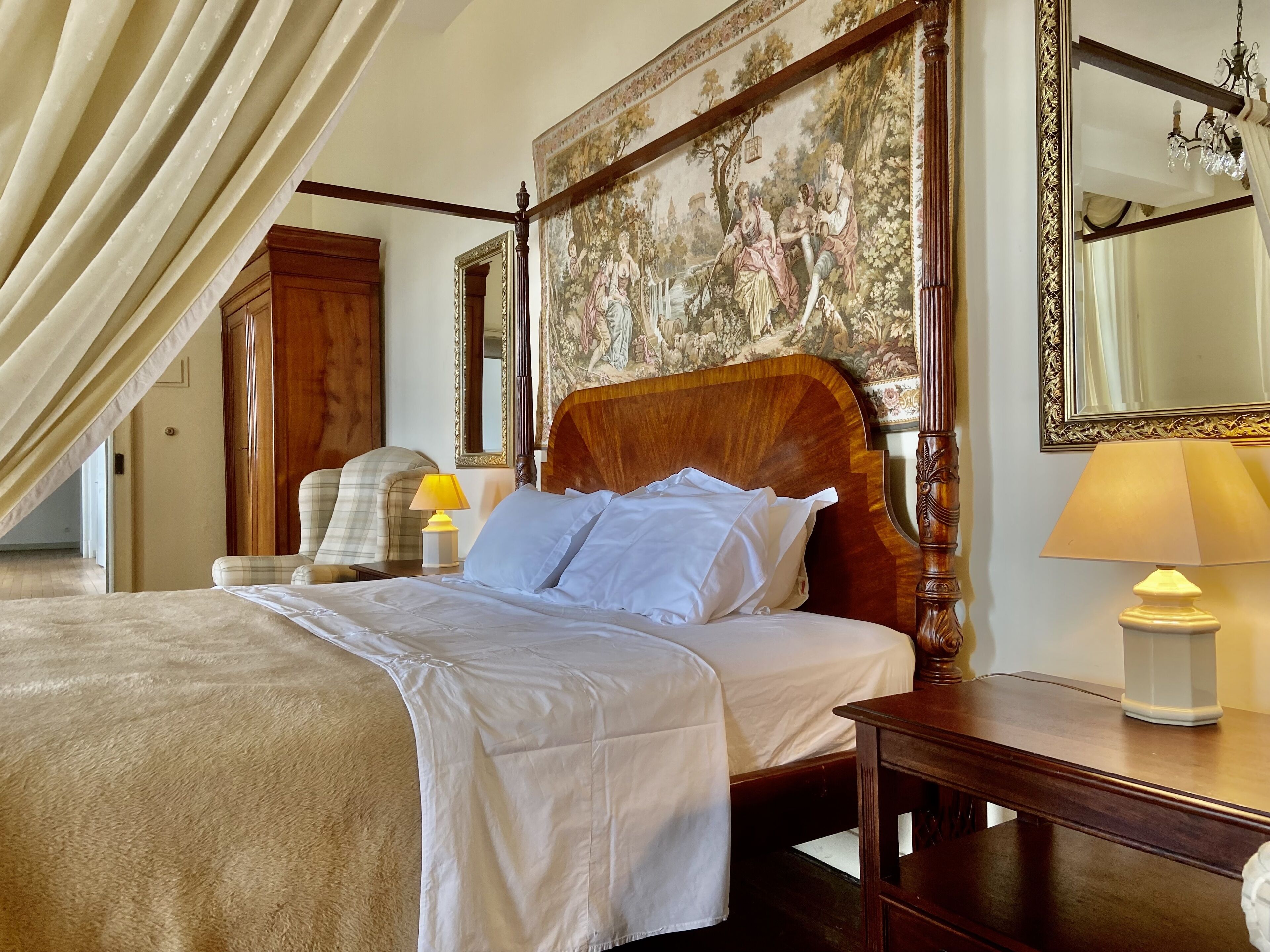 Een hotelkamer met een groot bed, een houten hoofdbord, een schilderij aan de muur en een kroonluchter.