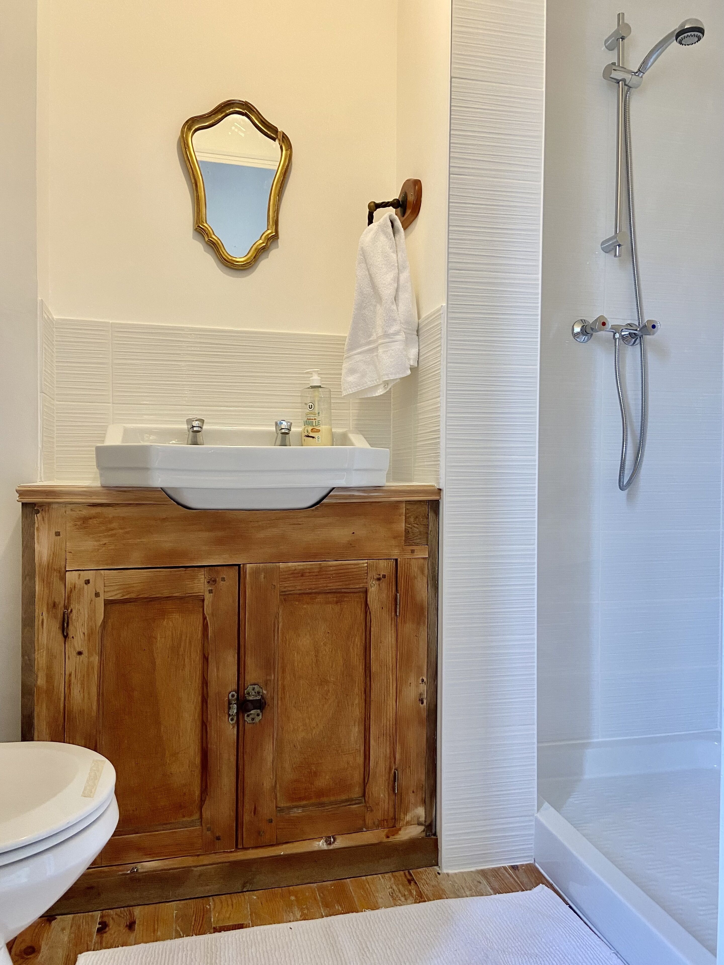A bathroom with a wooden vanity, a white sink, a mirror, and a shower.