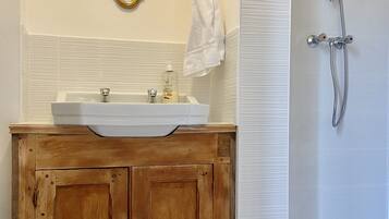 A bathroom with a wooden vanity, a white sink, a mirror, and a shower.