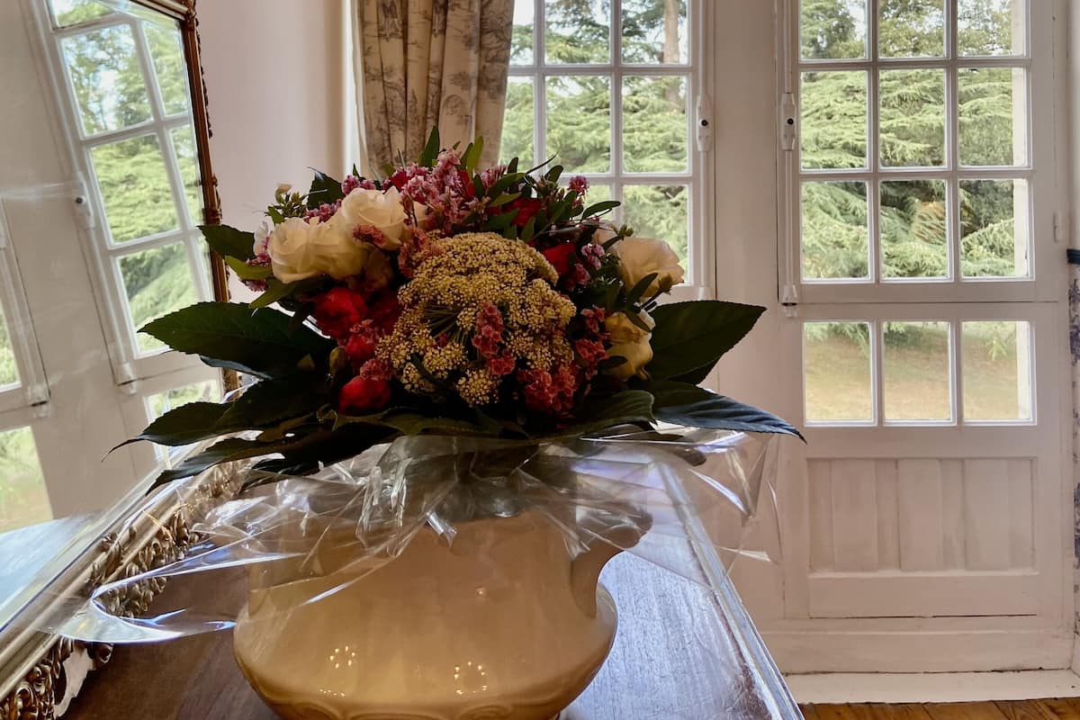A room with a large window, a door, and a vase with flowers on a table.