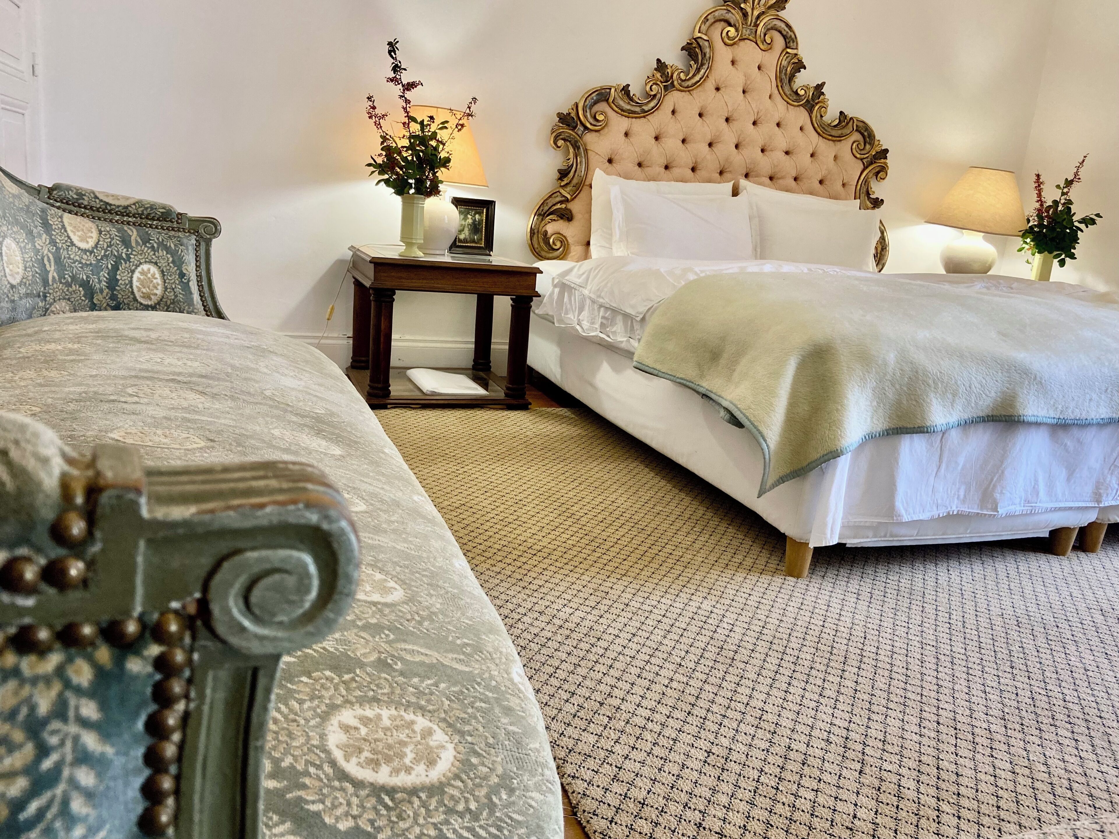 Un dormitorio con una cama grande, una cama más pequeña, una mesita de noche con una lámpara y un cabecero decorativo.