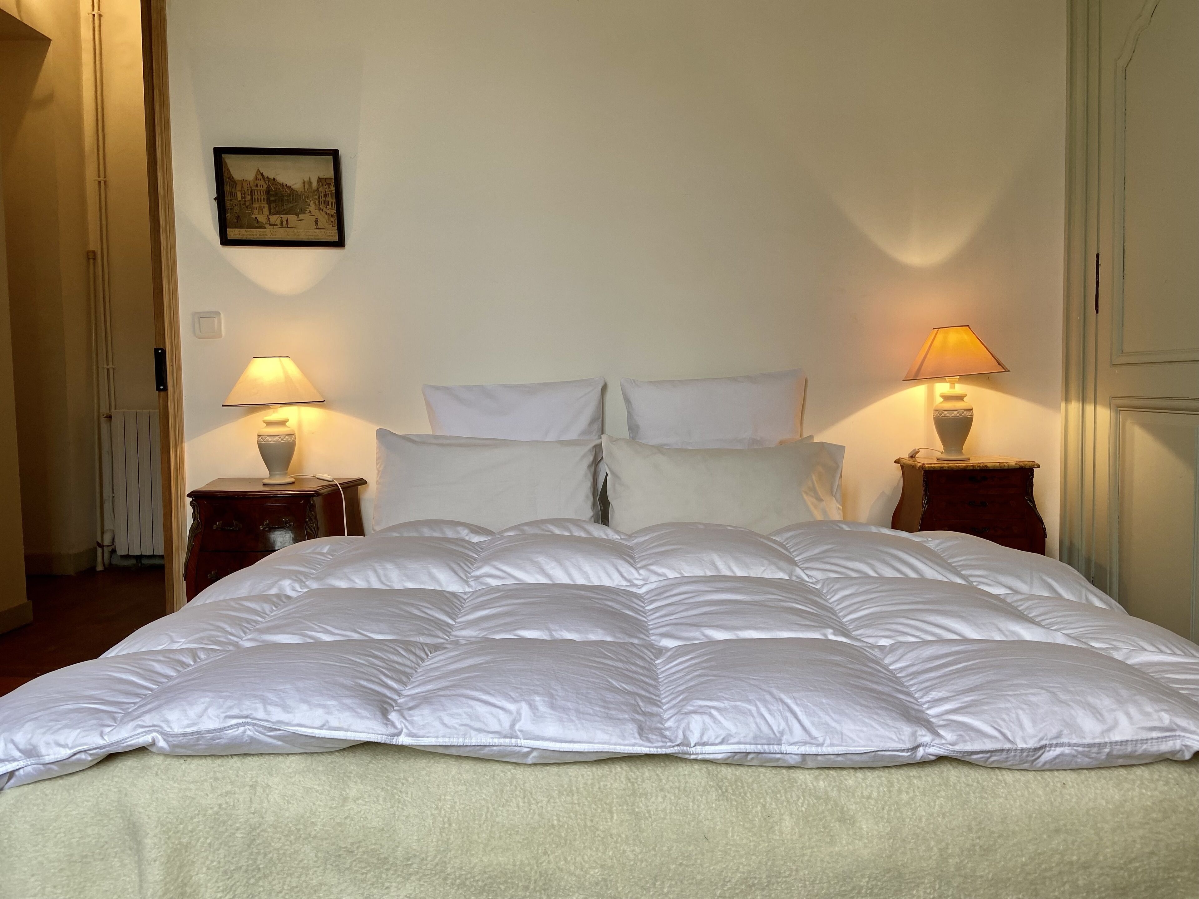 Un lit bien fait, avec une literie blanche, deux tables de chevet avec des lampes et un tableau encadré au mur.