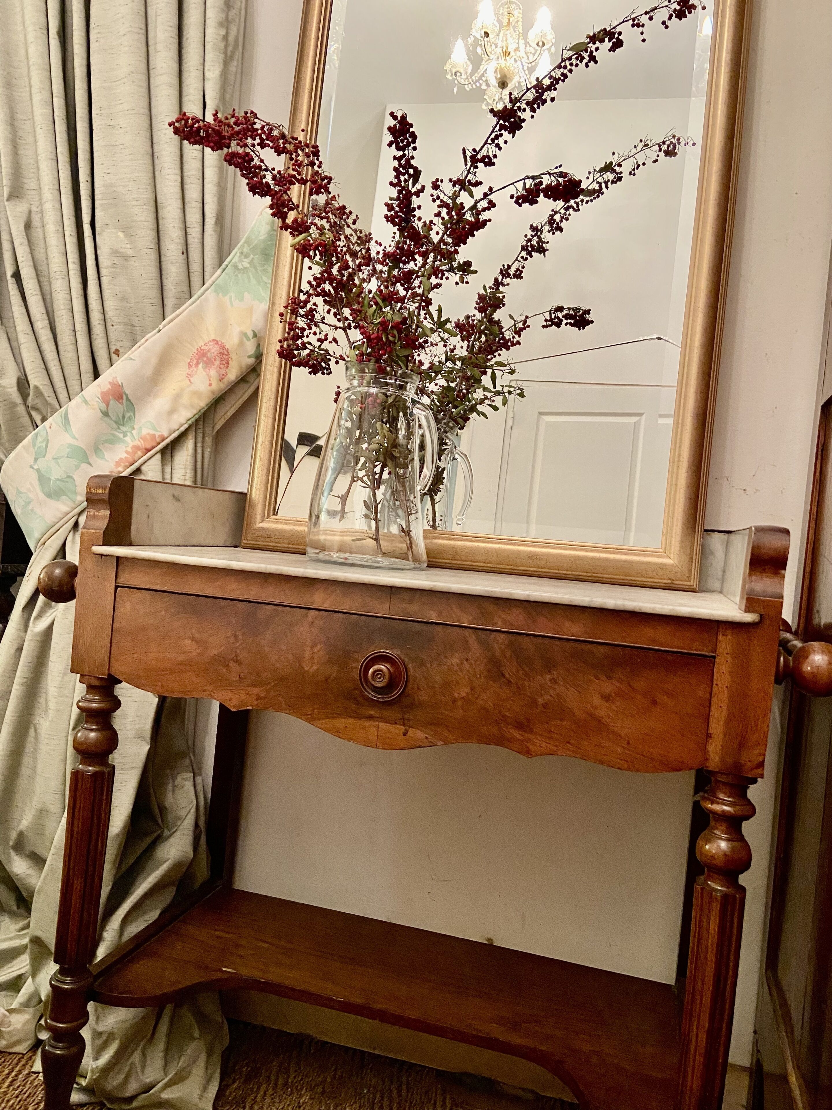 Une console en bois, agrémentée d’un miroir et d’un vase rempli de baies rouges.