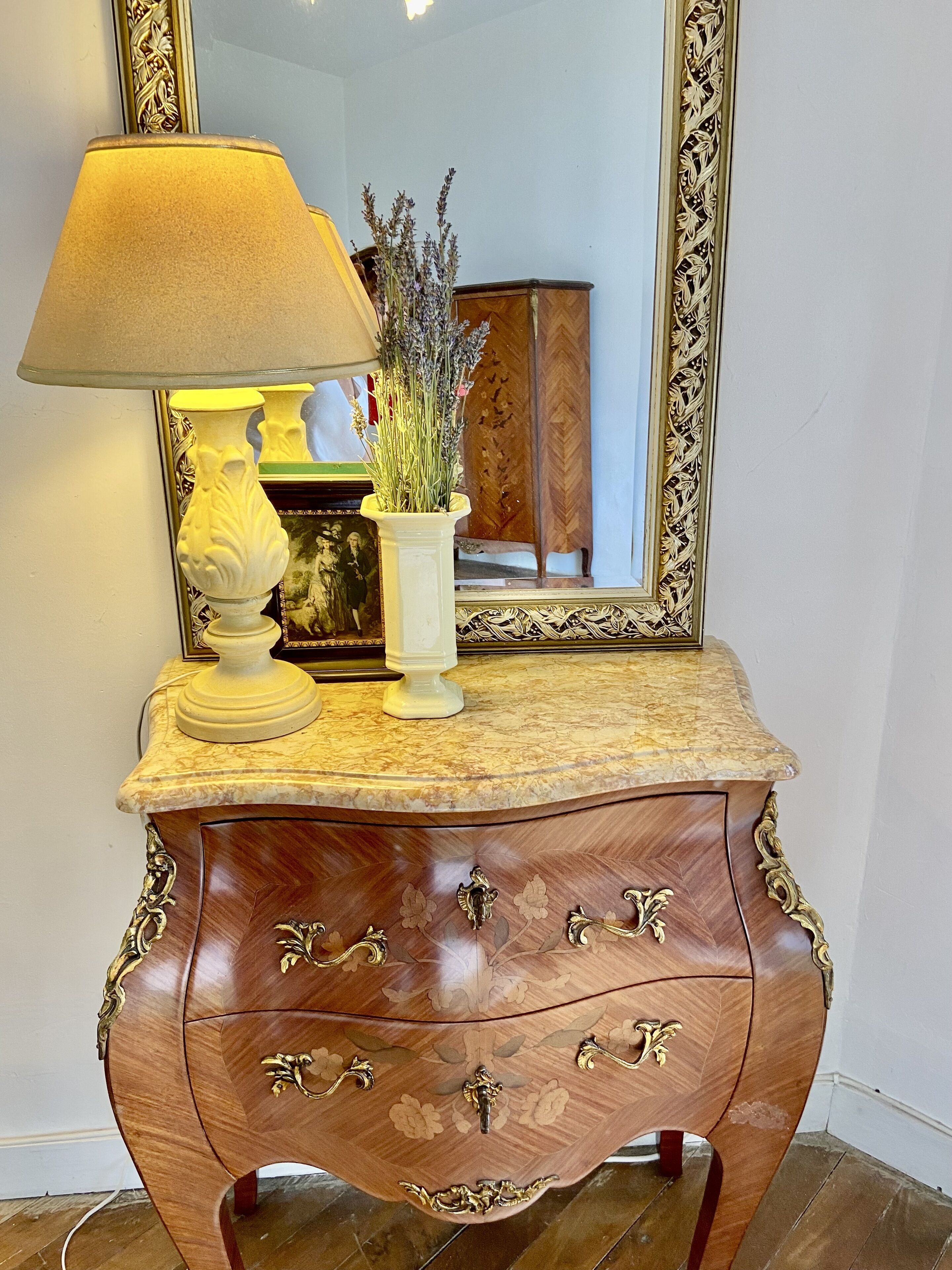 A wooden vanity with a marble top, a white vase with lavender, and a lamp.