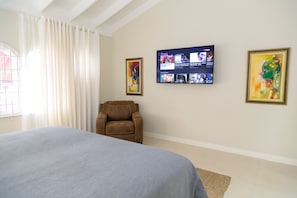 Ein Hotelzimmer mit Bett, Liegekorb, flachbildfernseher an der Wand und zwei gerahmten Kunstwerken.