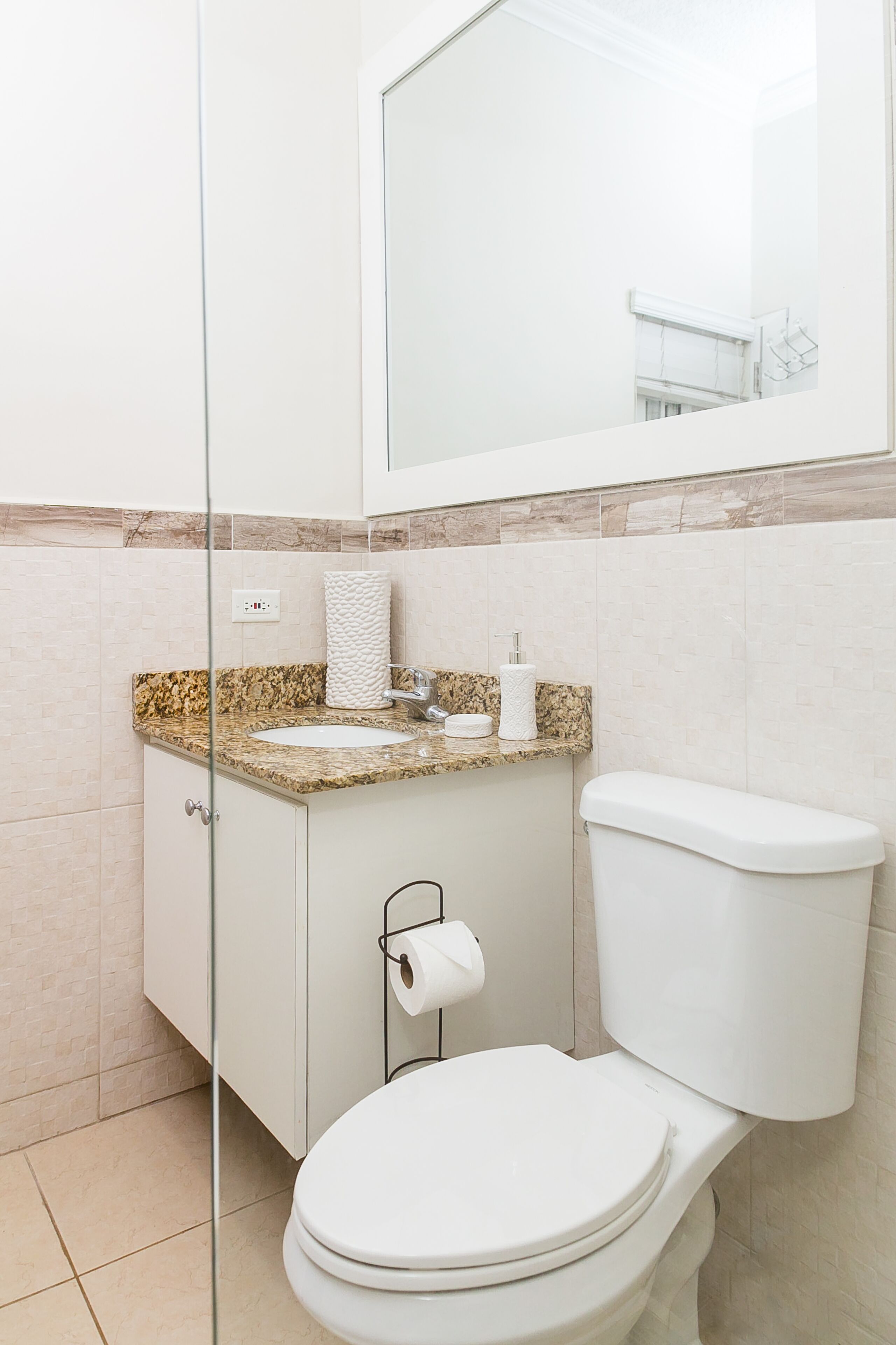A bathroom with a white toilet, a marble countertop sink, and a glass shower enclosure.