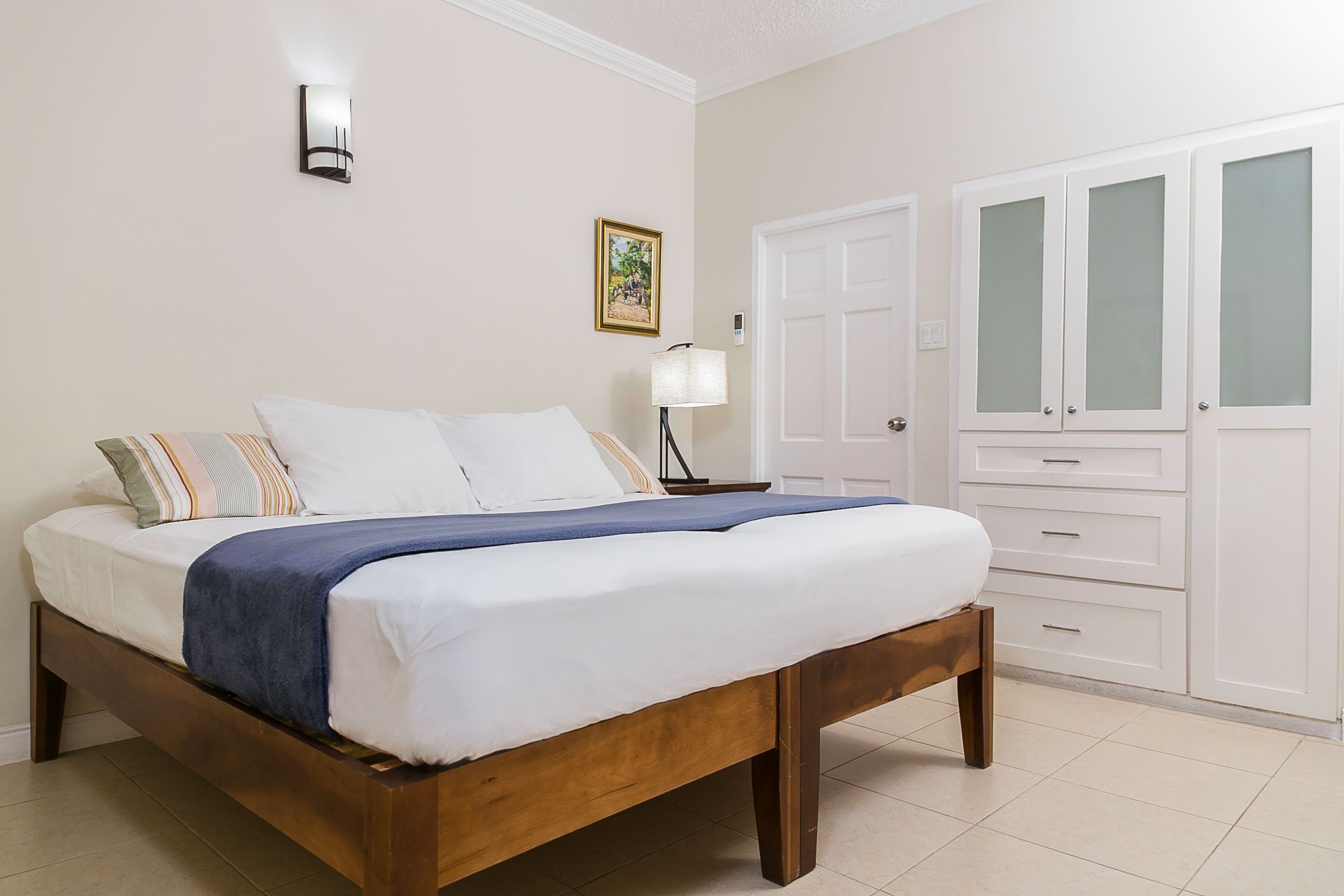A bedroom with a wooden bed, white walls, a bedside lamp, and a wardrobe with frosted glass doors.