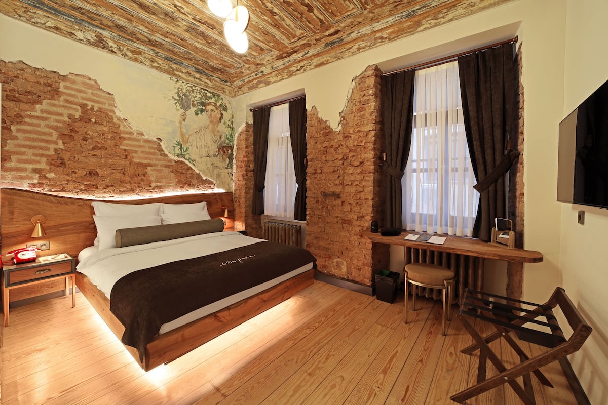 Een slaapkamer met zichtbare bakstenen muren, een houten bed, een bureau met stoel en een televisie aan de muur.