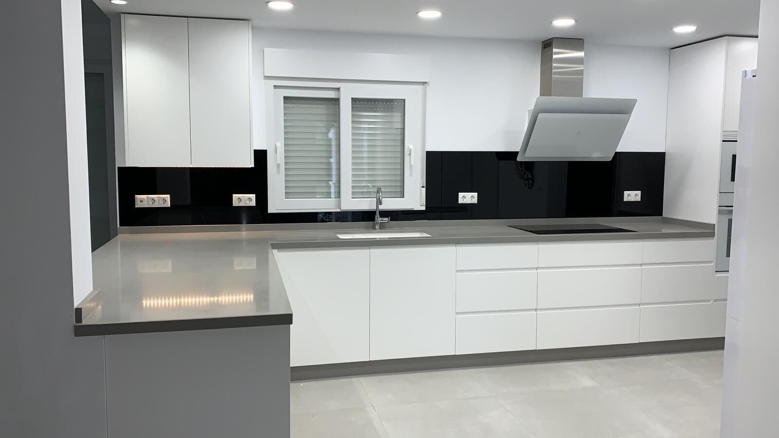 A modern kitchen with white cabinetry, a stainless steel range hood, and a window with blinds.