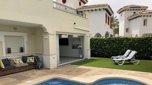 A swimming pool with a tiled edge, a covered outdoor seating area with a sofa, and a hedge in the background. - Modern 3 Bed Villa - Golf Side, Own Pool, sleeps 6, Mar Menor Golf Resort     (Torre-Pacheco)