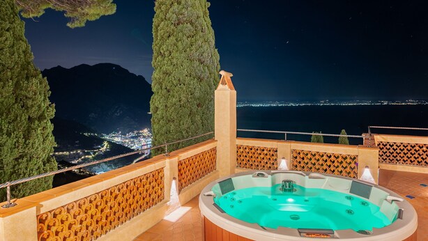A hot tub with a panoramic view of a city and mountains at night. - Villa Barluzzi (Ravello)