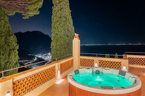 A hot tub with a panoramic view of a city and mountains at night. - Villa Barluzzi (Ravello)