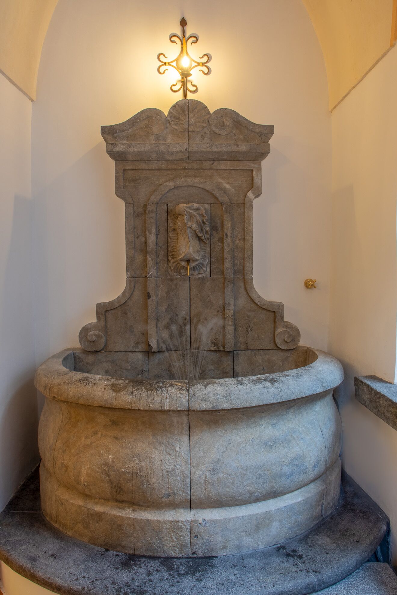 Ein Steinkunstbrunnen mit verziertem Oberteil und einer zentralen Skulptur.