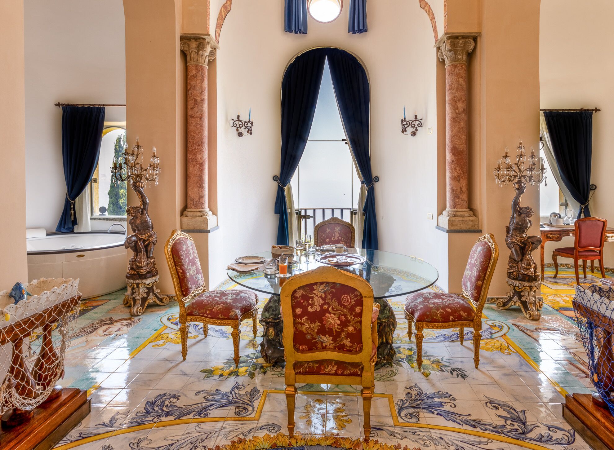 A luxurious dining room with ornate chairs, a glass table, and a view of the outdoors through a large window.