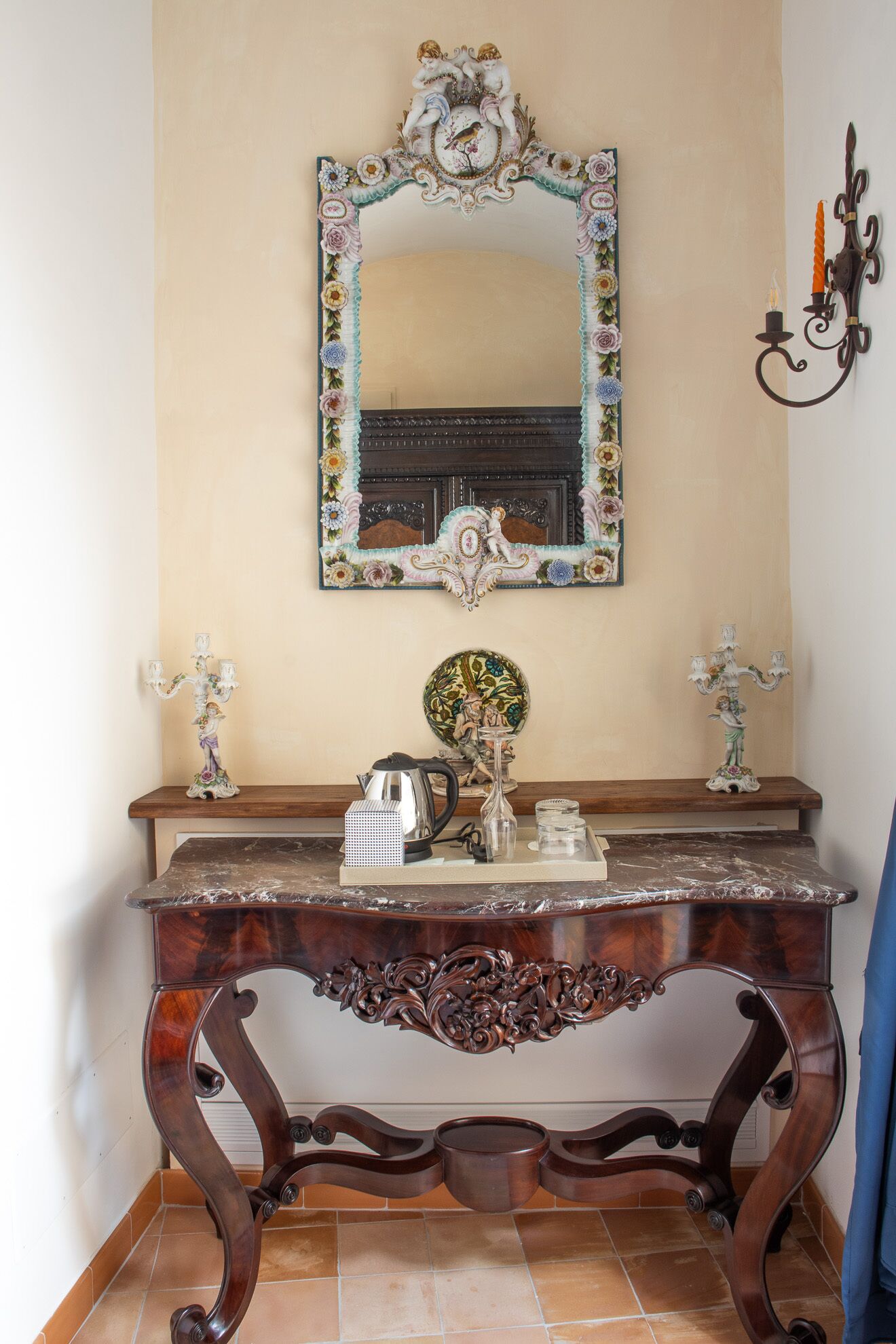 A wooden console table with a mirror above it, flanked by two wall-mounted candelabras.