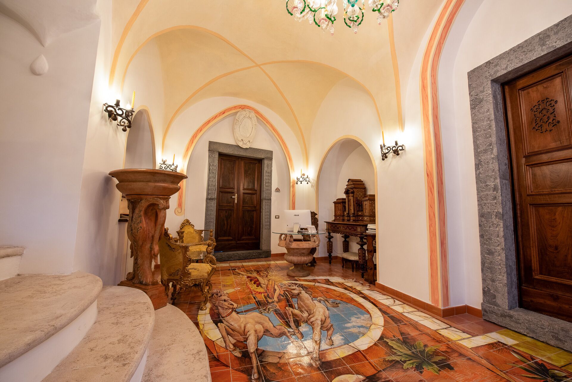 A grand hallway with a tiled floor, a large wooden door, and a chandelier.