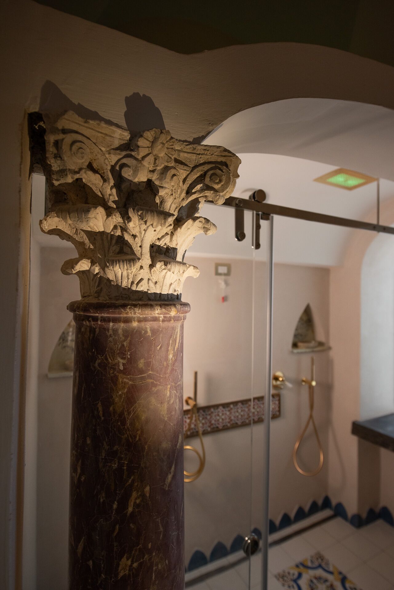 Una colonna di marmo con elaborate decorazioni, una zona doccia con porta in vetro e un pavimento decorato.