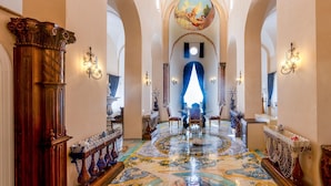 A grand hallway with ornate columns, a patterned floor, and a view into a brightly lit room. - Villa Barluzzi (Ravello)