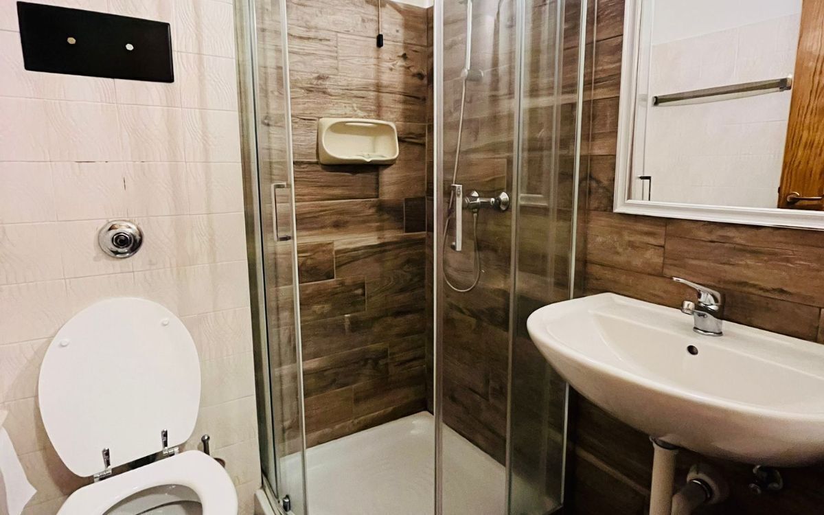 A bathroom with a glass-enclosed shower, a toilet, and a sink.
