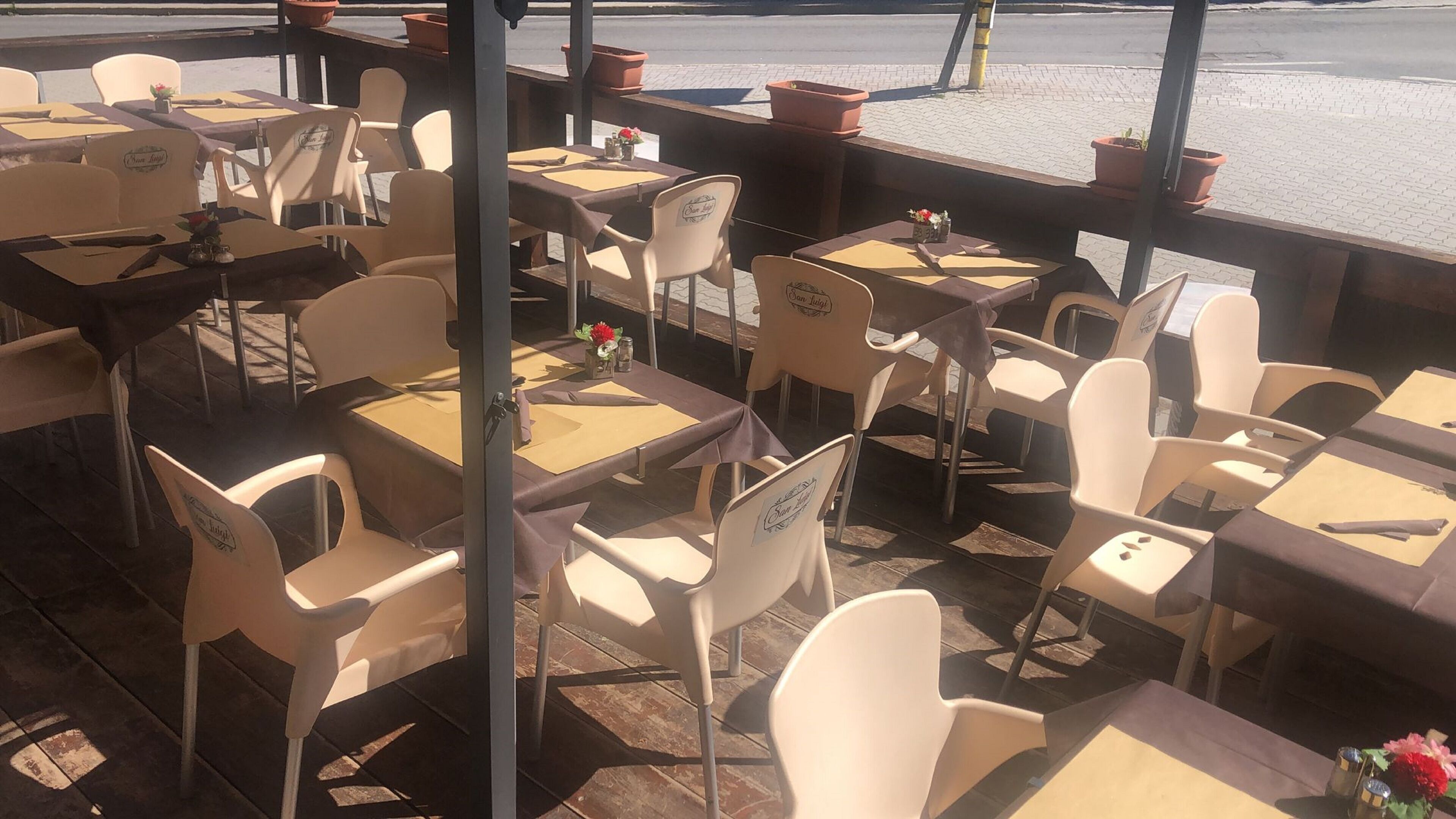 Un café al aire libre con mesas y sillas, algunas con la marca 'San Luis'.