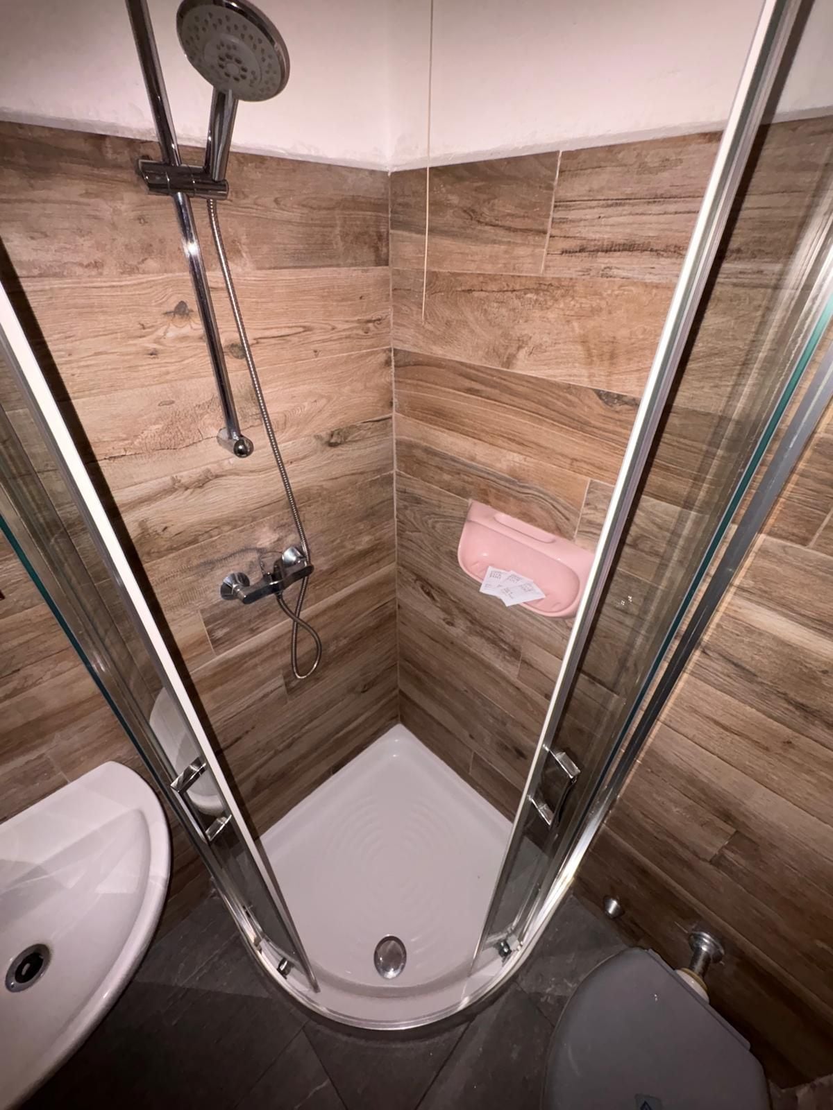 Cabina de ducha con puerta de vidrio, ducha de mano y rociador manual.