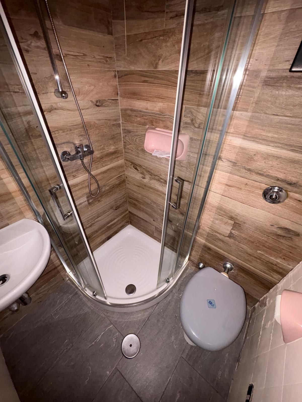 A small bathroom with a glass-enclosed shower, a white sink, and a toilet.