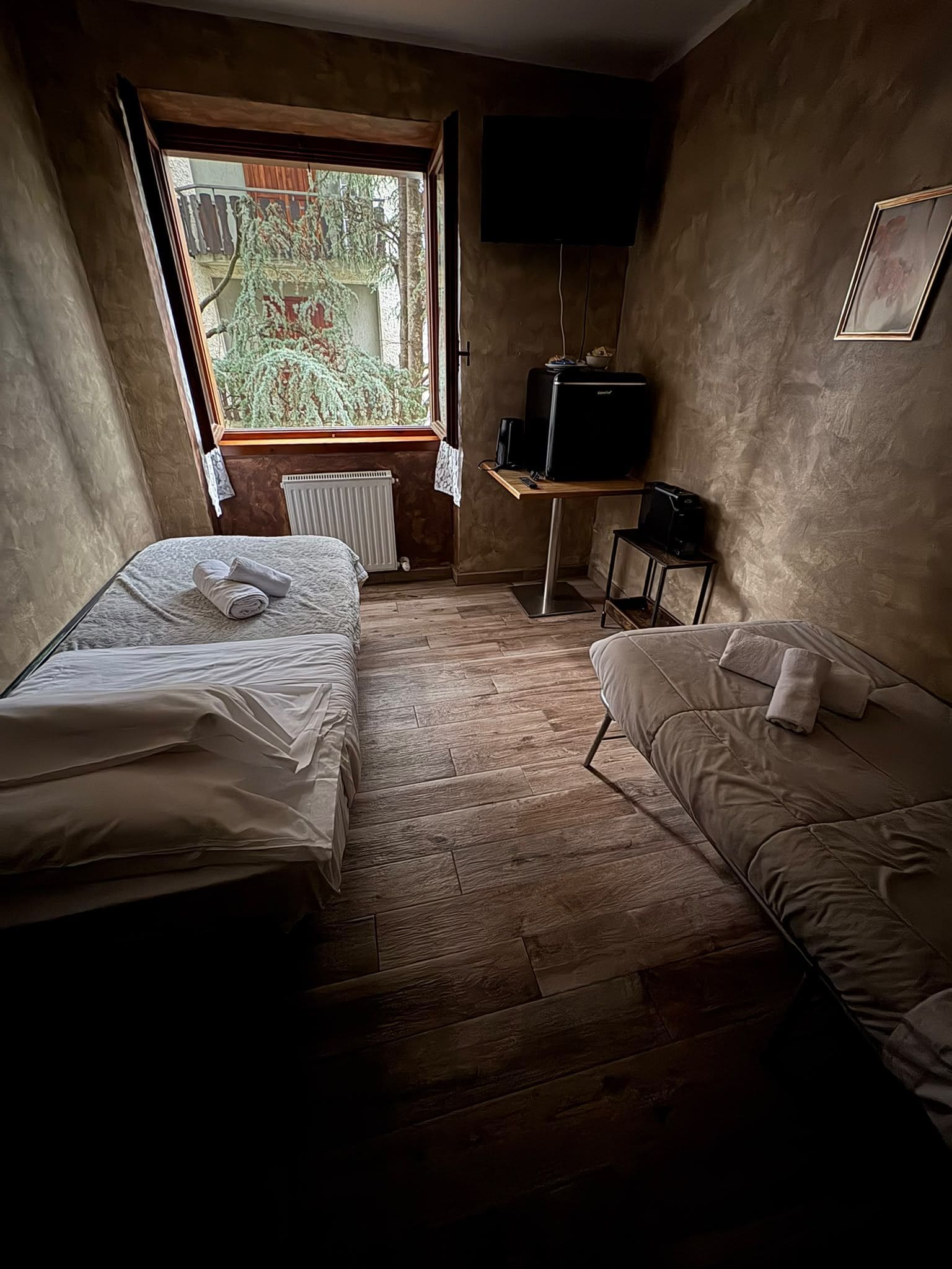 Una habitación con cama, sofá, televisión y ventana con vistas a árboles.