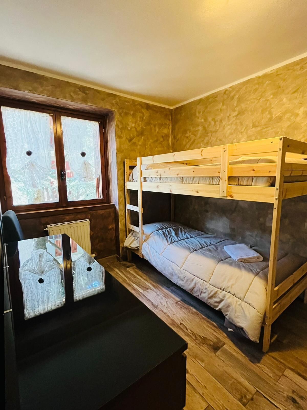 Ein Schlafraum mit Etagenbetten, einem Fenster, einem Heizkörper und einem kleinen Tisch mit Lampe.